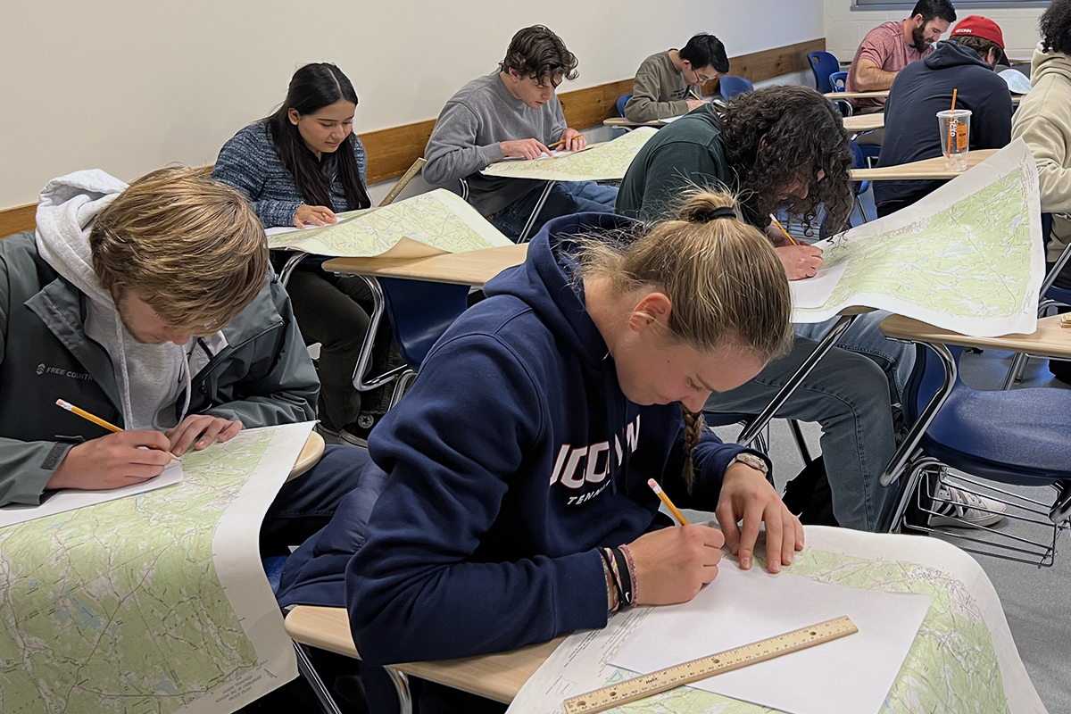 Students drawing on maps in a classroom.
