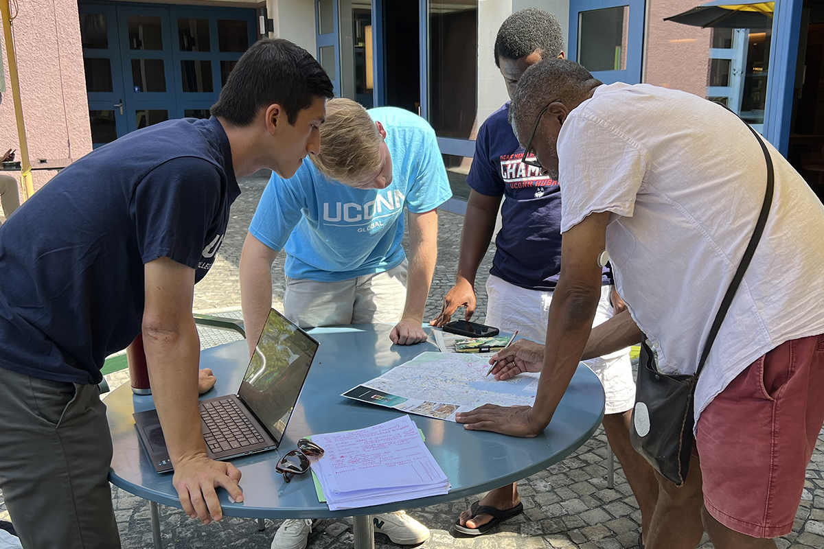 A professor points to a piece of paper while collaborating with students outside.